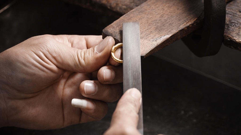 A goldsmith filing a gold ring by hand at the workbench